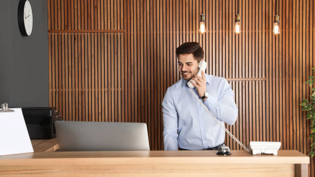 A receptionist taking a phone call at a hotel front desk.
