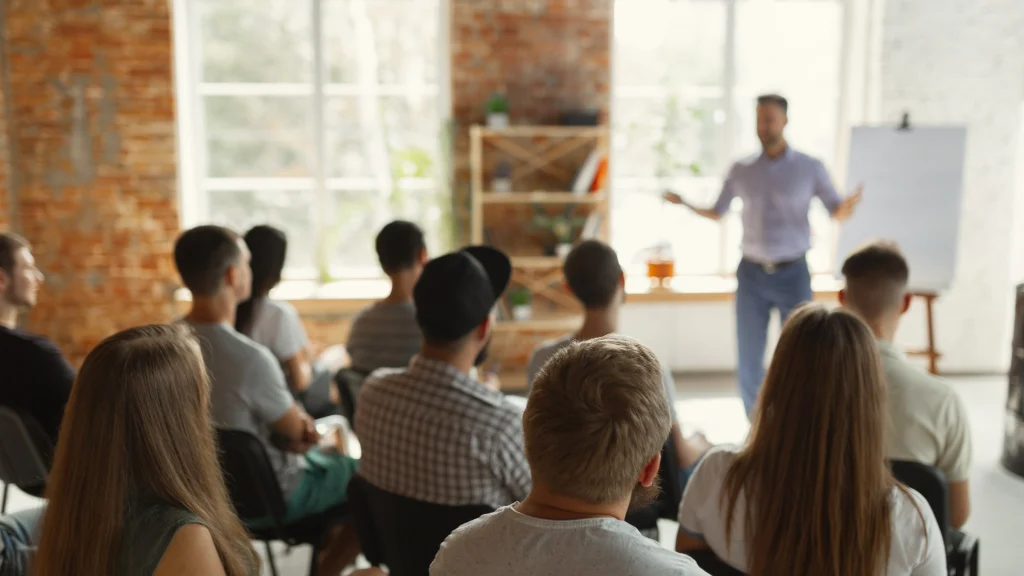 People seated at a workshop, listening to a presenter at the front of the room.